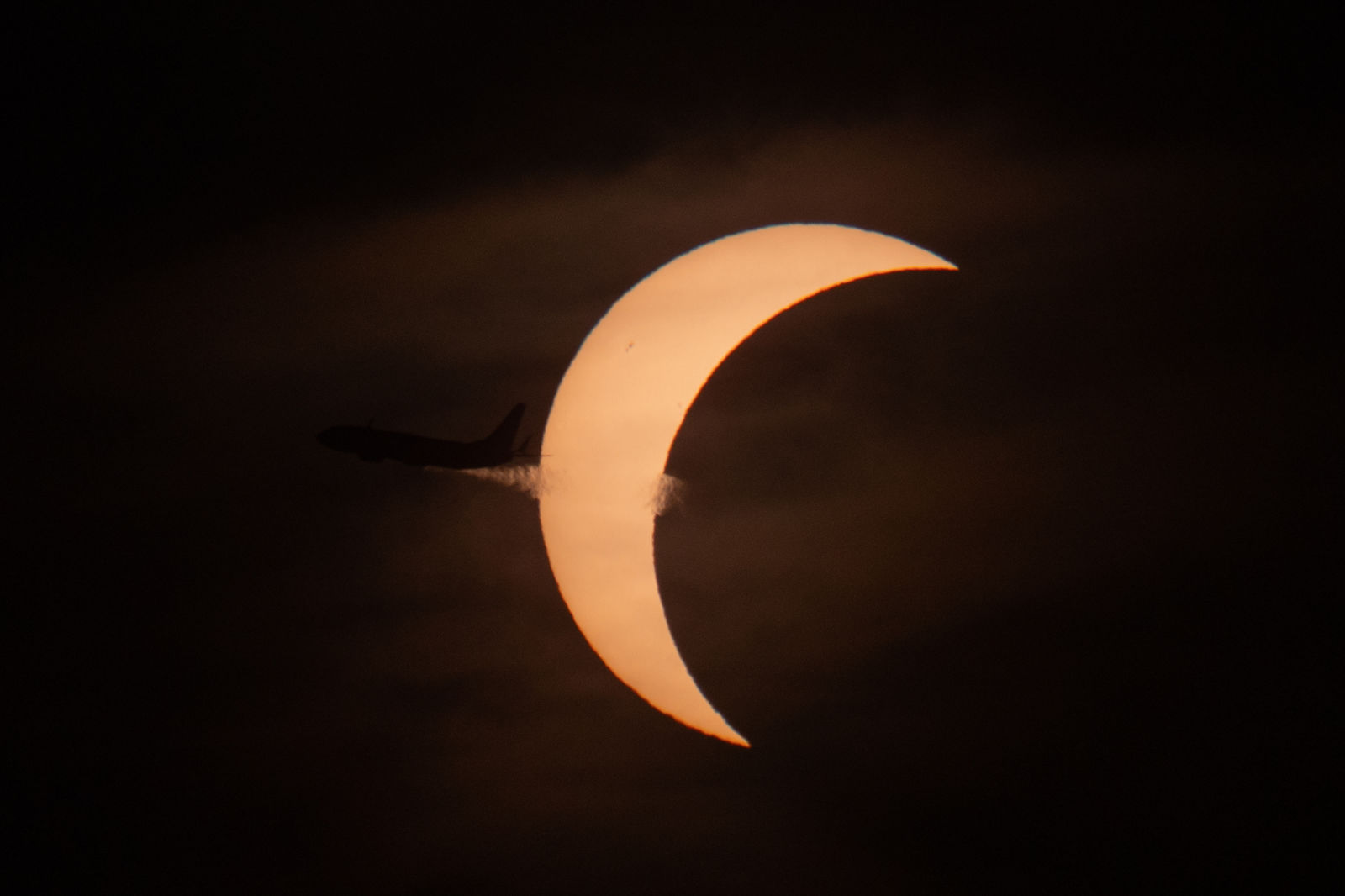 The same aircraft a moment later, vapour trail streaming across the crescent sun.